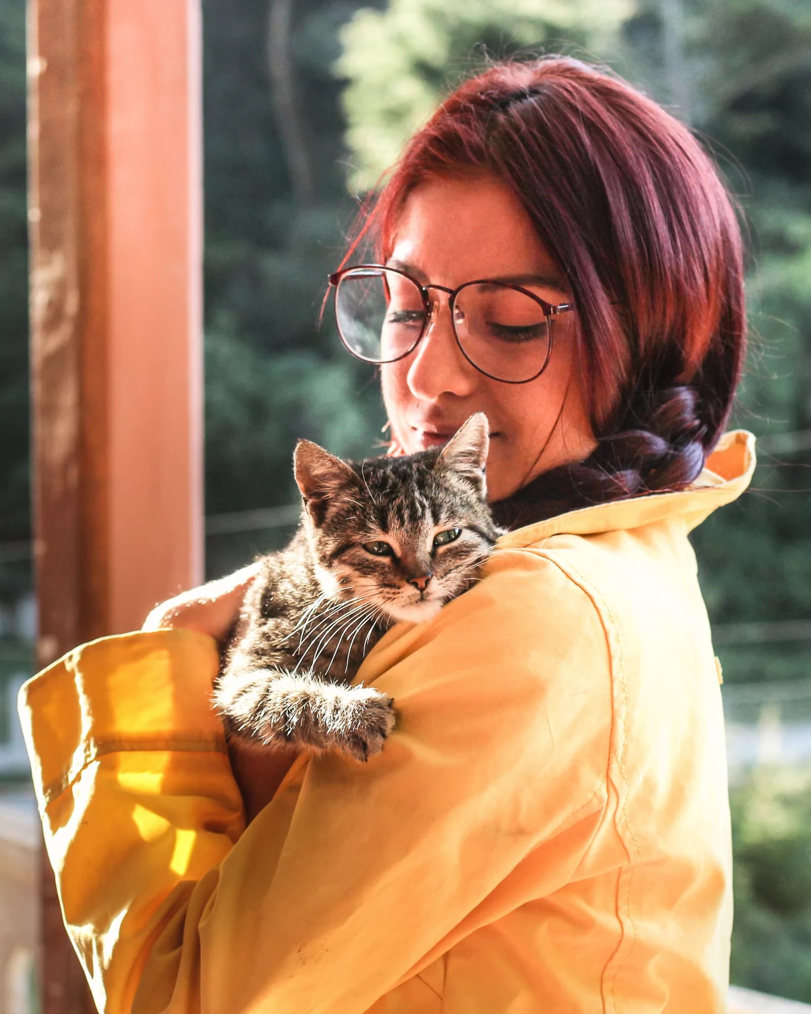 A woman in a yellow jacket cradling a tabby cat on her shoulder